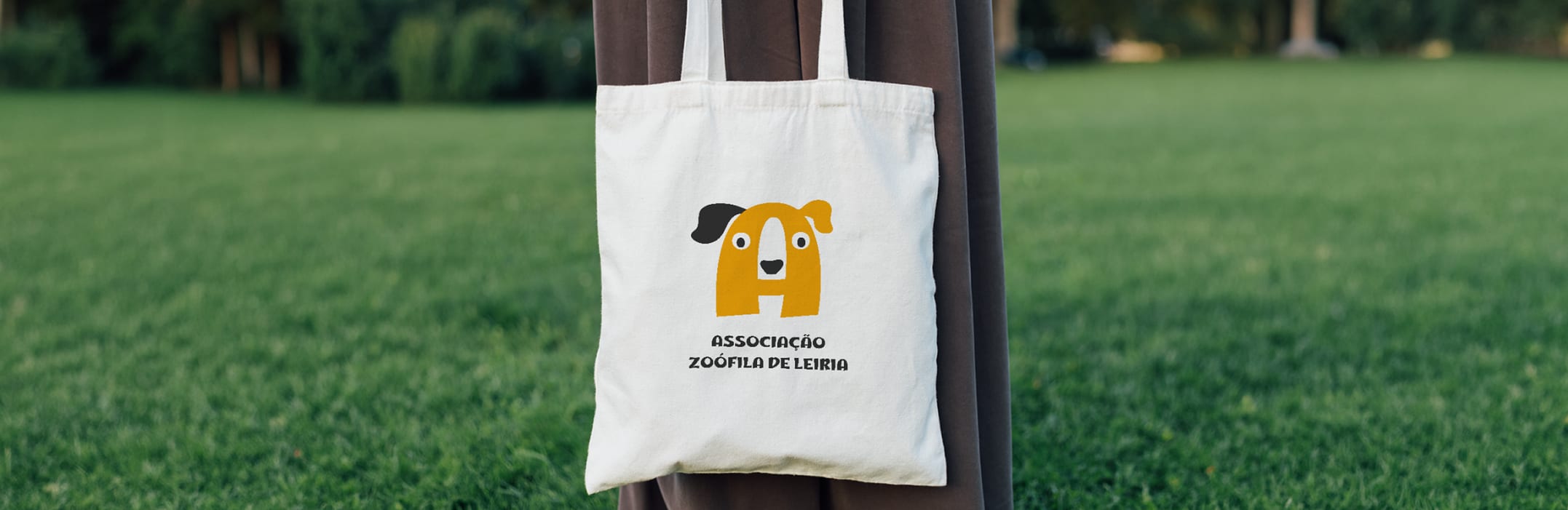 White AZL tote bag hanging on a tree trunk in a park