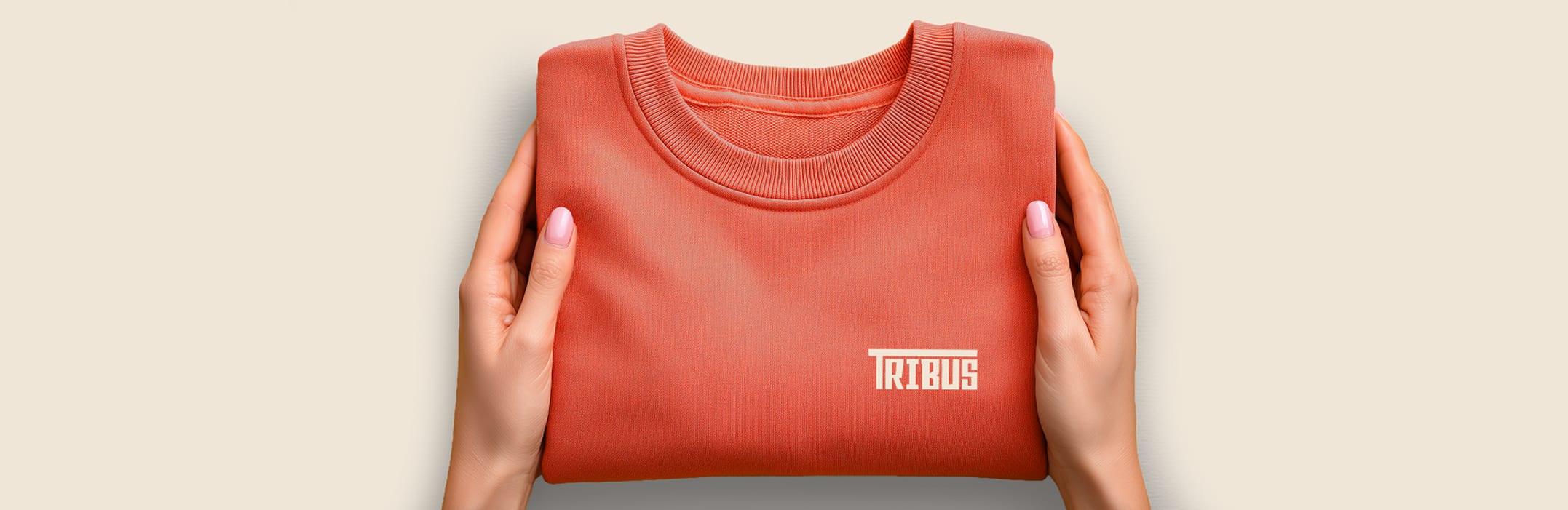 Hands holding a folded clay-red Tribus t-shirt with the wordmark