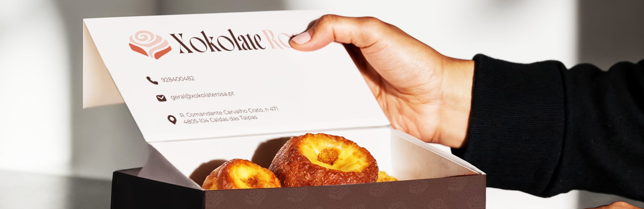 Hand opening a Xokolate Rosa pastry box with printed contact details